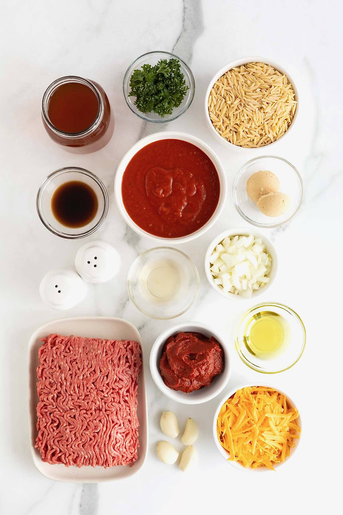 Ingredients to make Sloppy Joe Orzo in small glass dishes on a white marble counter.