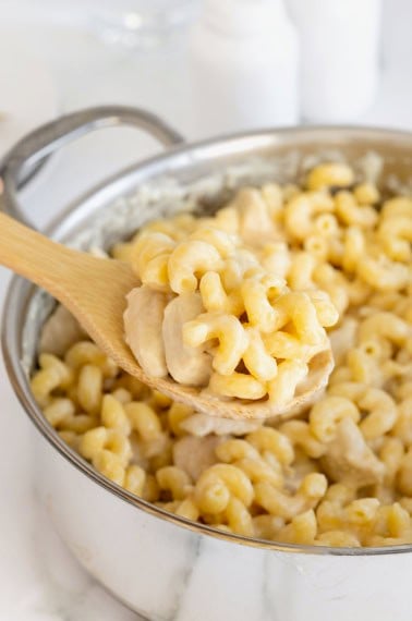 A wooden spoon scooping chicken Alfredo pasta from a stainless steel pot.