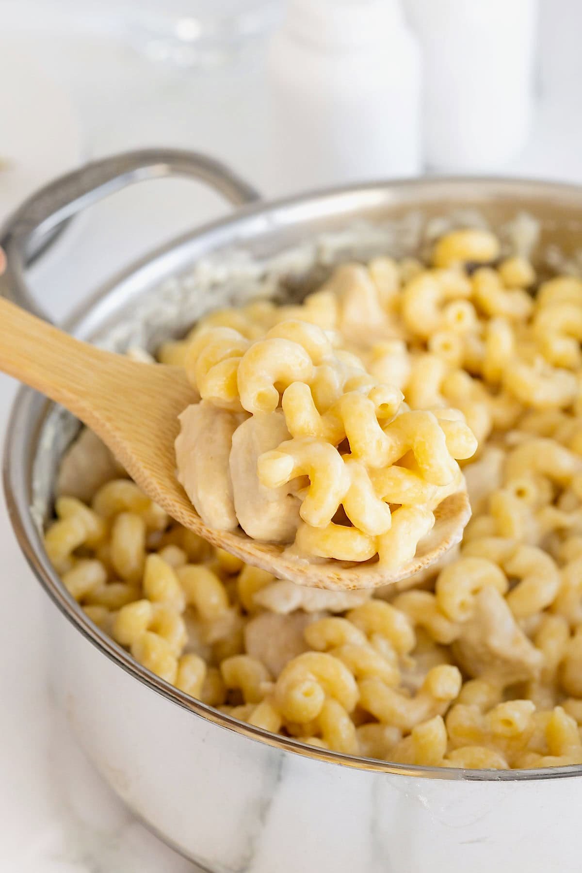 A wooden spoon scooping chicken Alfredo pasta from a stainless steel pot.