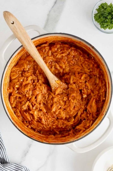 A white Dutch oven of sloppy Joe orzo on a white marble counter.