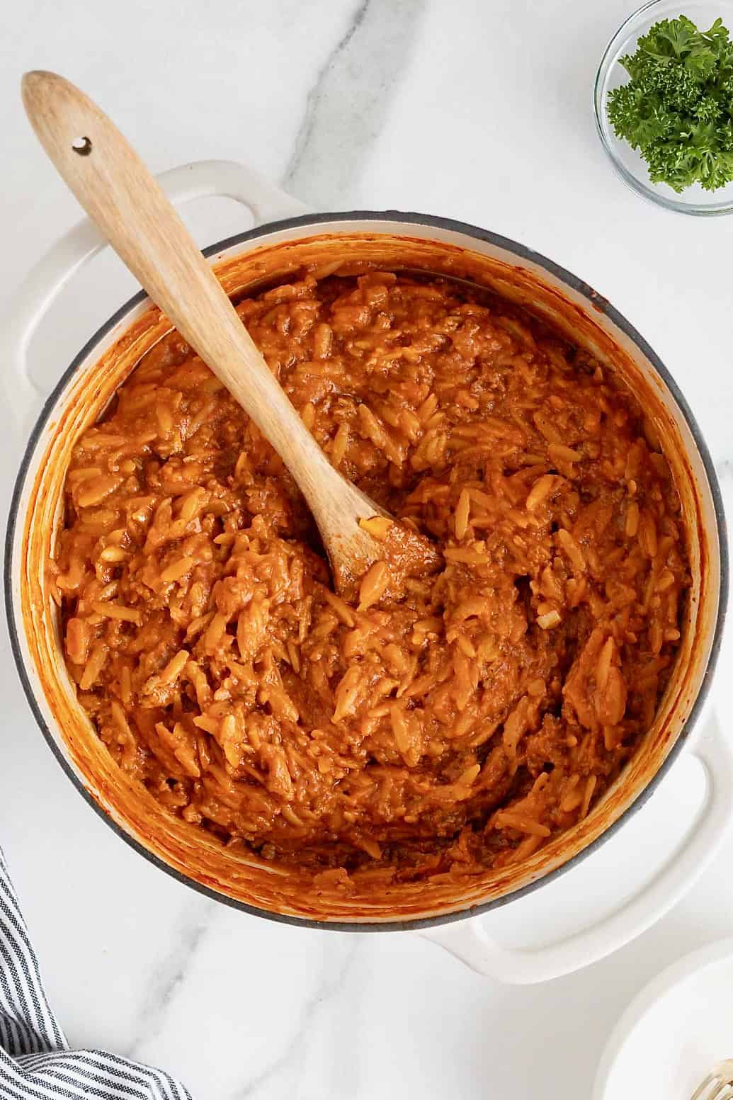 A white Dutch oven of sloppy Joe orzo on a white marble counter.