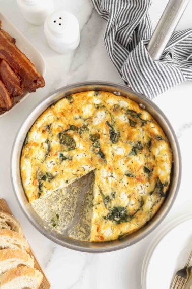 A spinach and goat cheese frittata in an aluminum pan on a white marble counter.