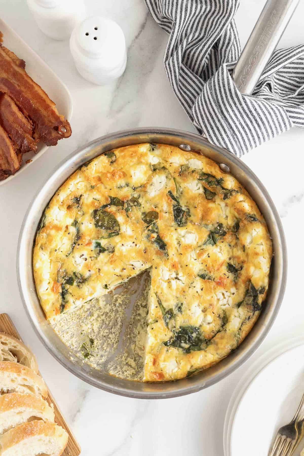 A spinach and goat cheese frittata in an aluminum pan on a white marble counter.