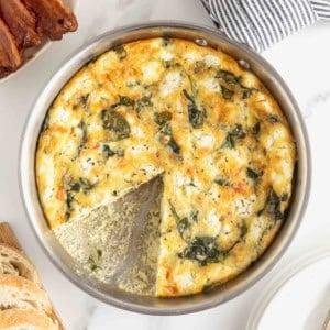 A spinach and goat cheese frittata in stainless steel skillet on a white marble counter.