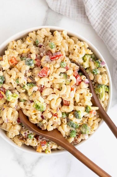 A large white serving bowl of macaroni salad with sweet peas, red onion and cheese.