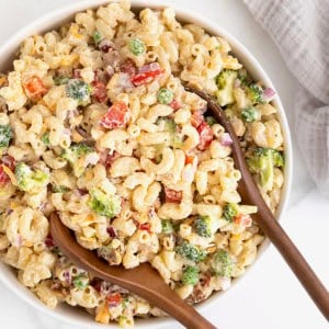 A large white serving bowl of macaroni salad with sweet peas, red onion and cheese.