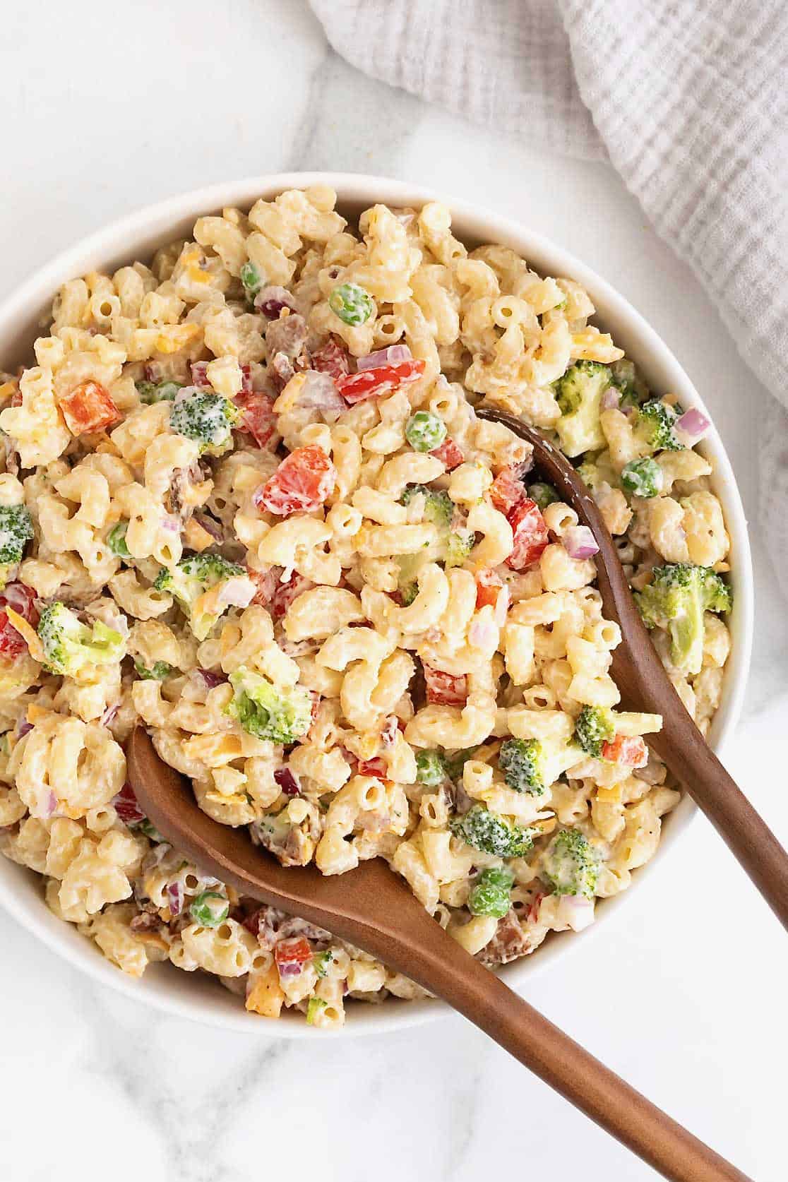 A large white serving bowl of macaroni salad with sweet peas, red onion and cheese.