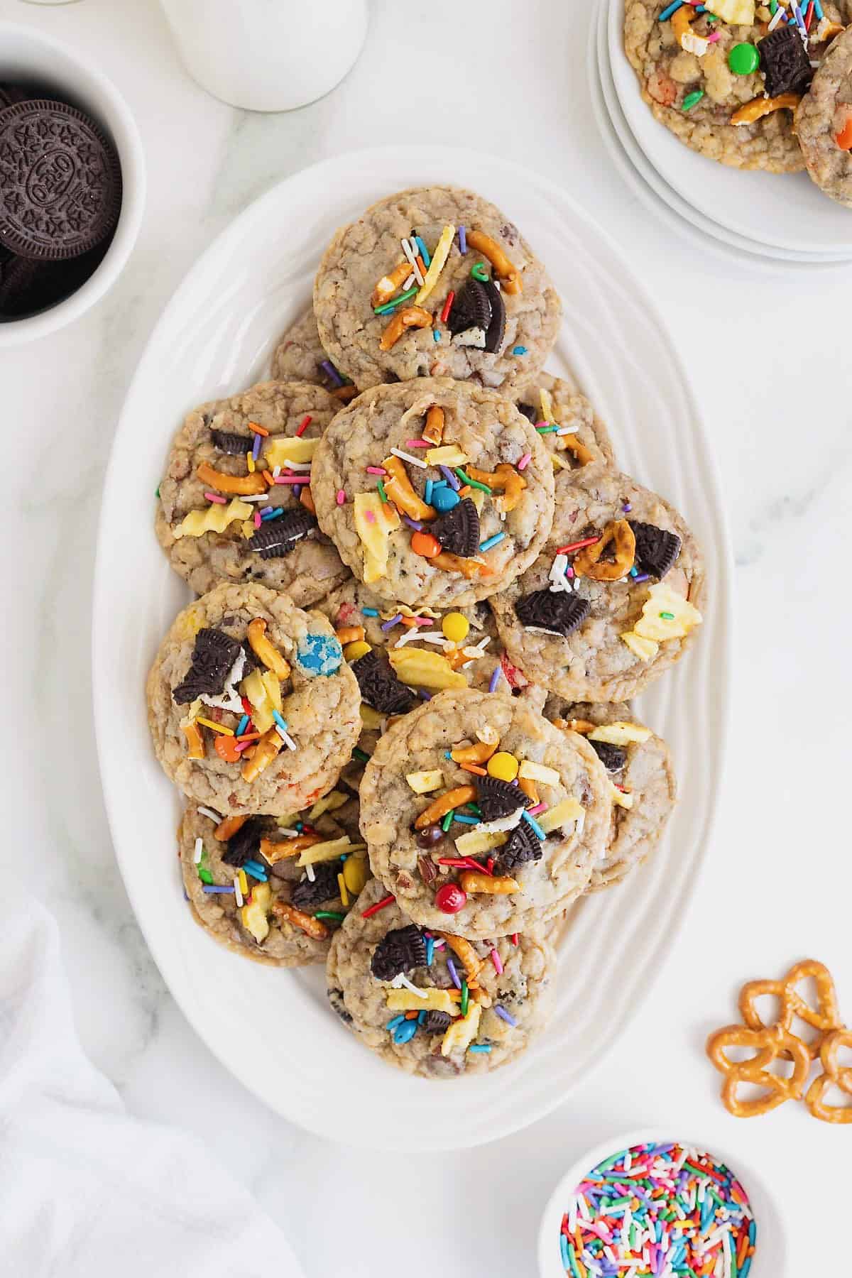 An oblong white serving plate filled with Kitchen Sink cookies on a white marble counter.