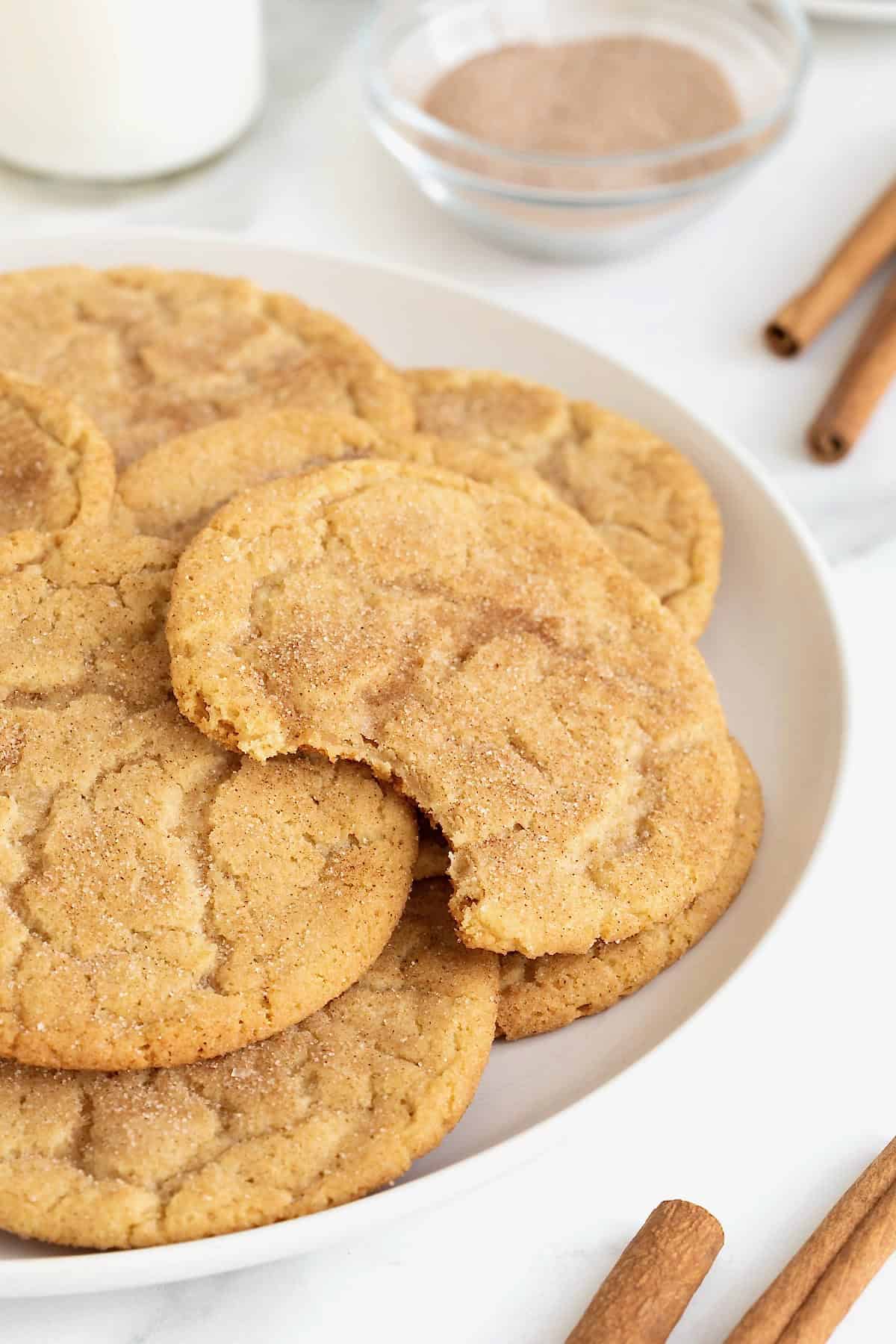 A bite taken out of a snickerdoodle cookie on a plate of cookies.