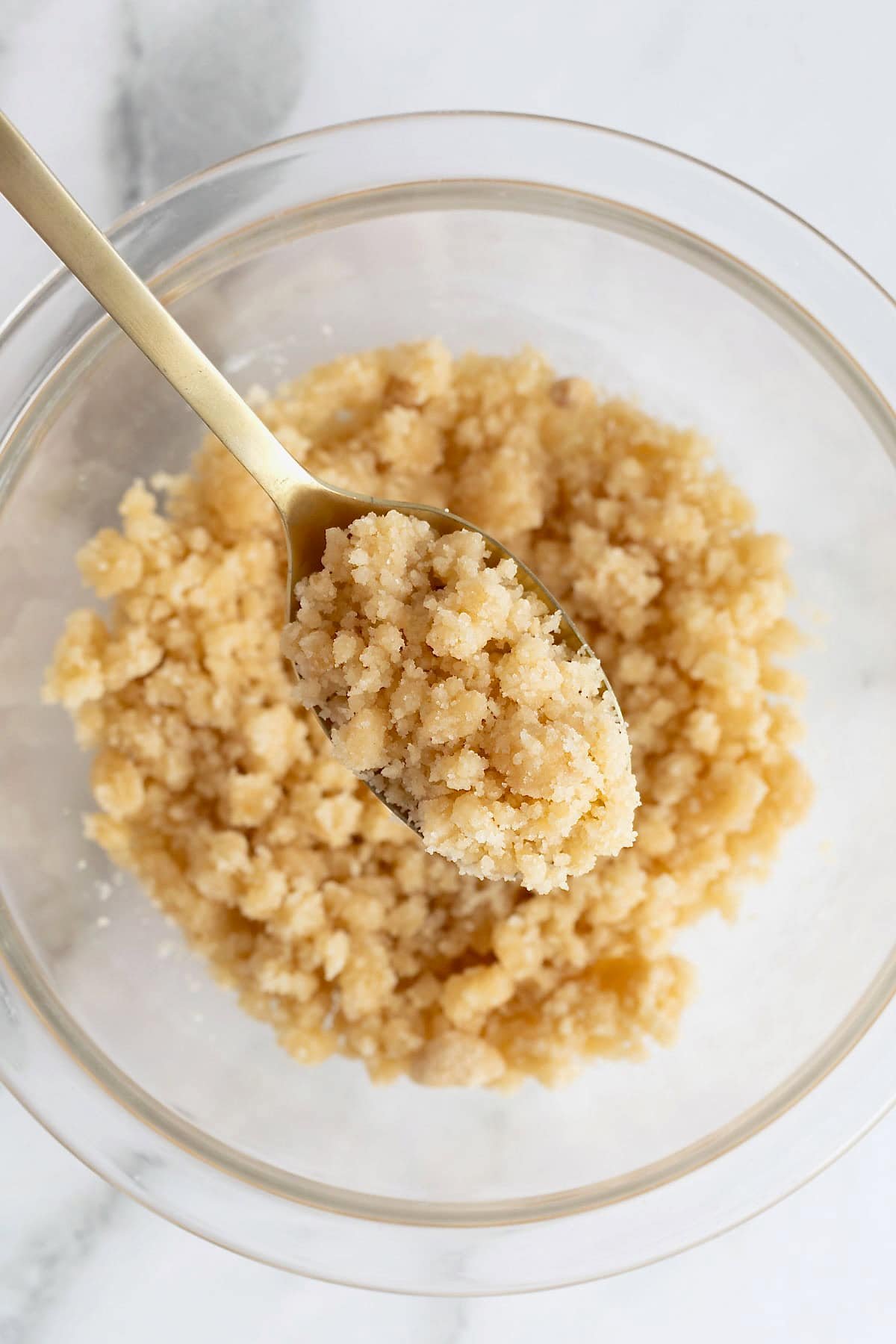 A spoonful of streusel being lifted from a glass bowl.