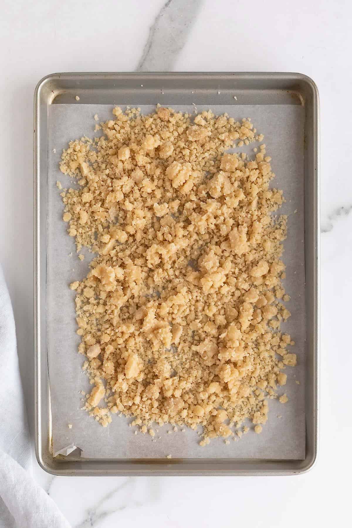 Streusel on a parchment lined baking sheet on a white marble counter.
