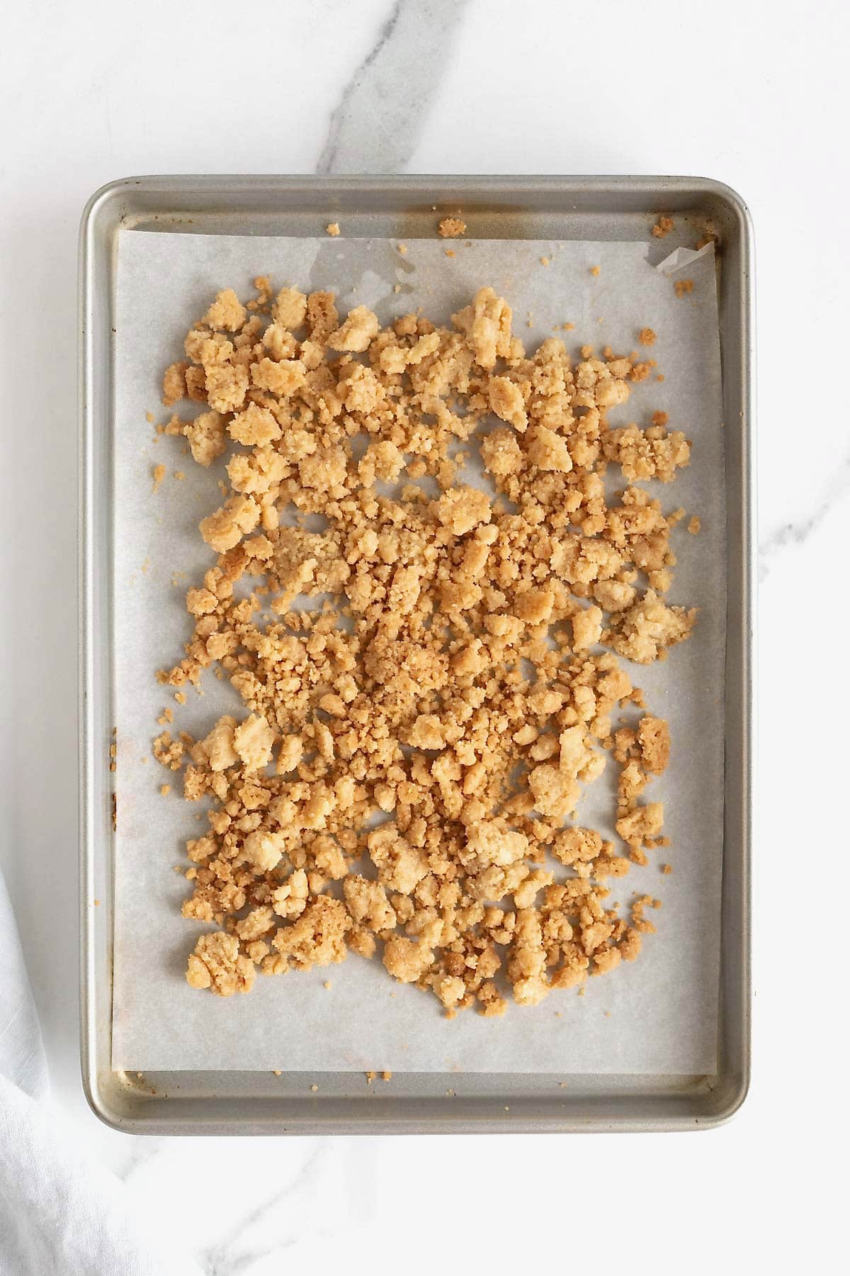 Baked streusel on a parchment lined baking sheet on a white marble counter.