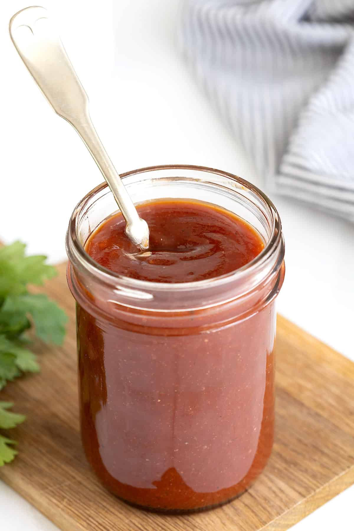 A wide mouth glass jar of barbecue sauce with a spoon sticking out of it.