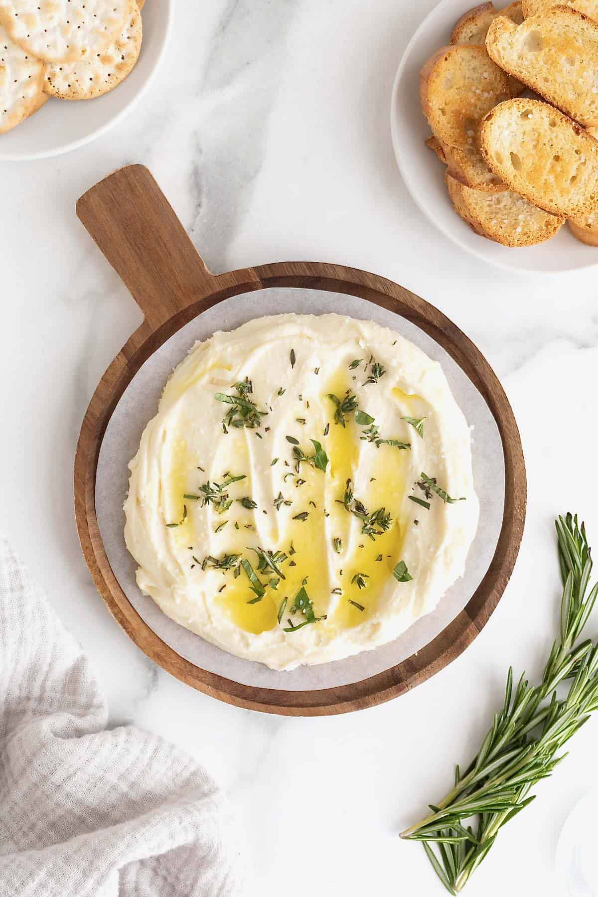 Whipped brie on a wooden serving plate drizzled with olive oil and sprinkled with fresh herbs.