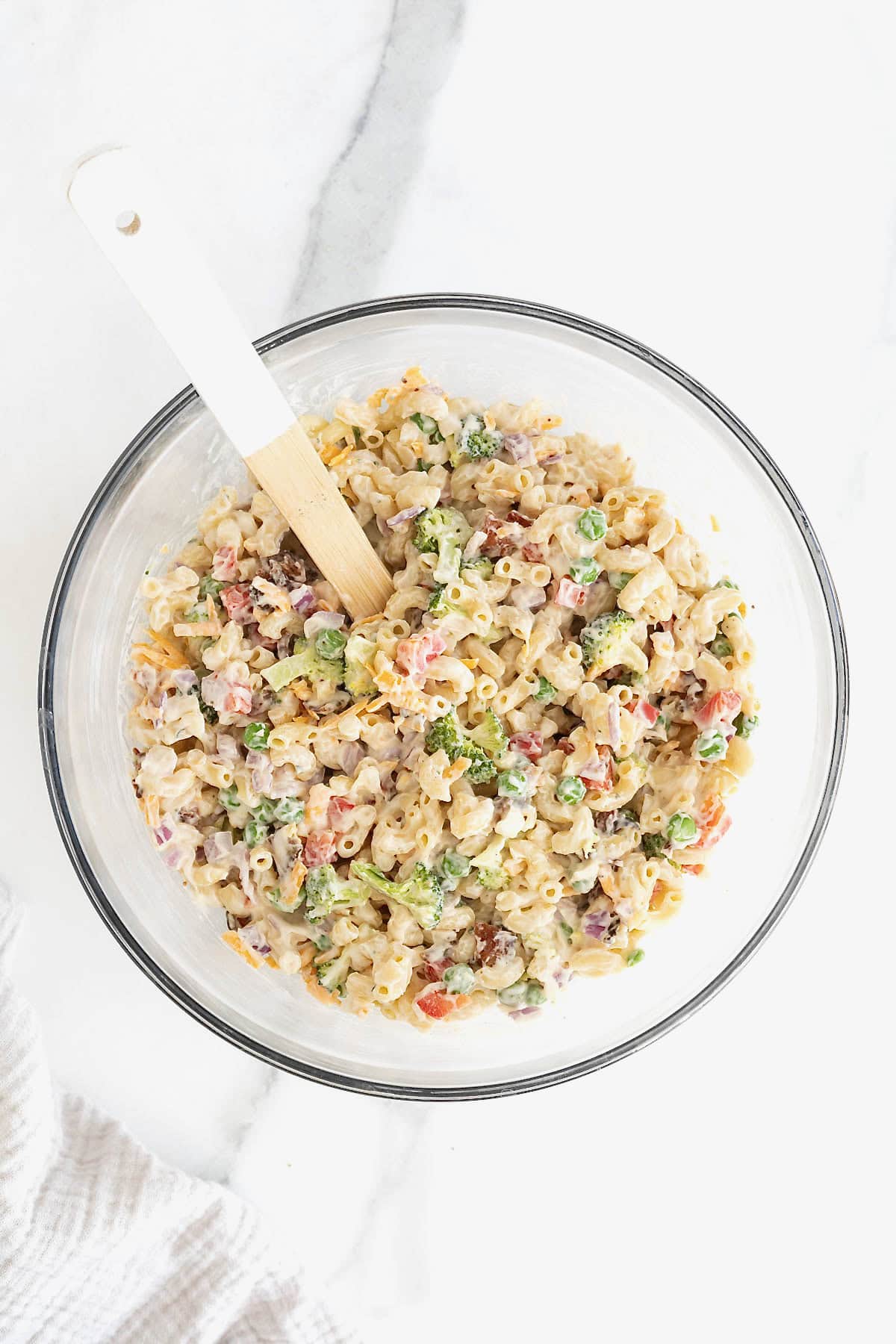 Bacon ranch macaroni salad in a large glass mixing bowl with a white handled wooden spoon sticking out.