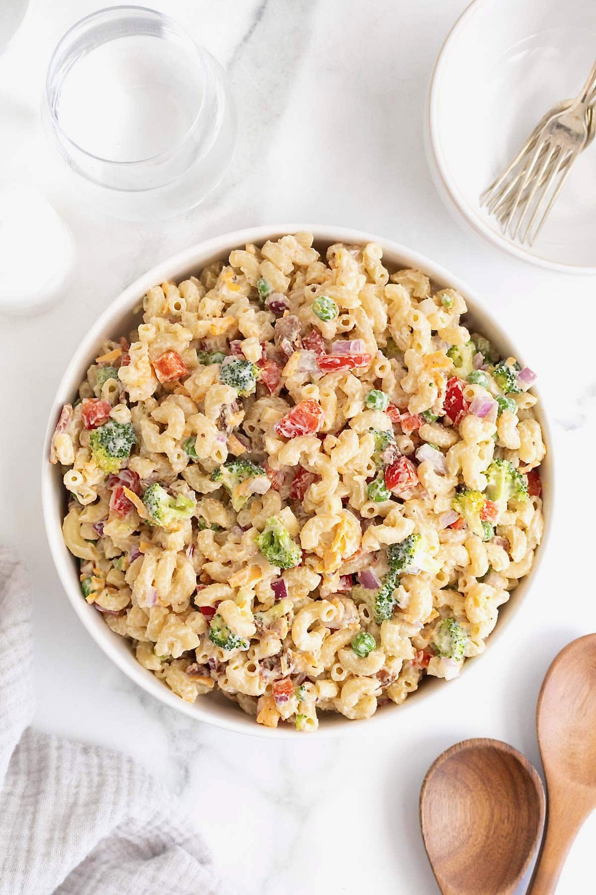 Macaroni salad in a large white serving bowl on a white marble counter.