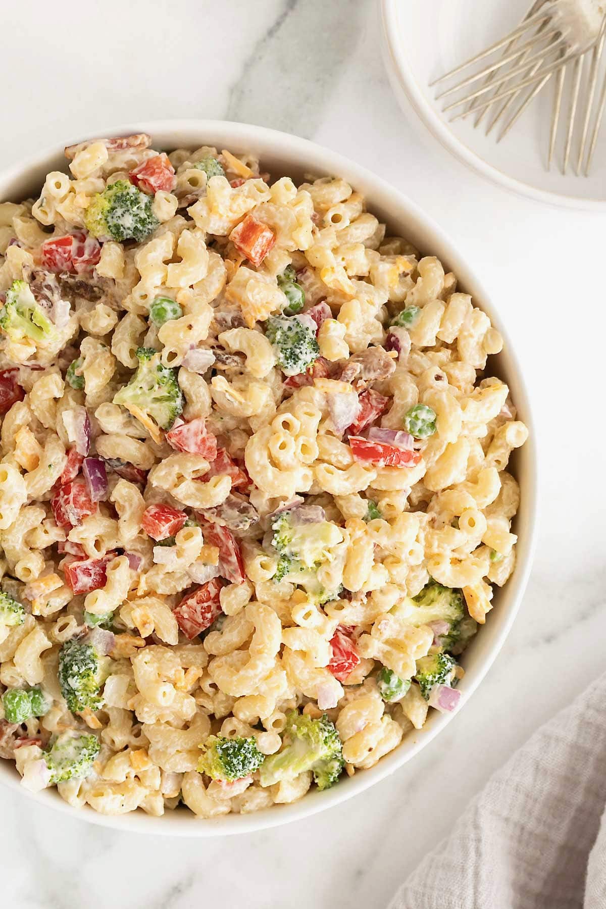 A large white serving bowl of macaroni salad with sweet peas, red onion and cheese.