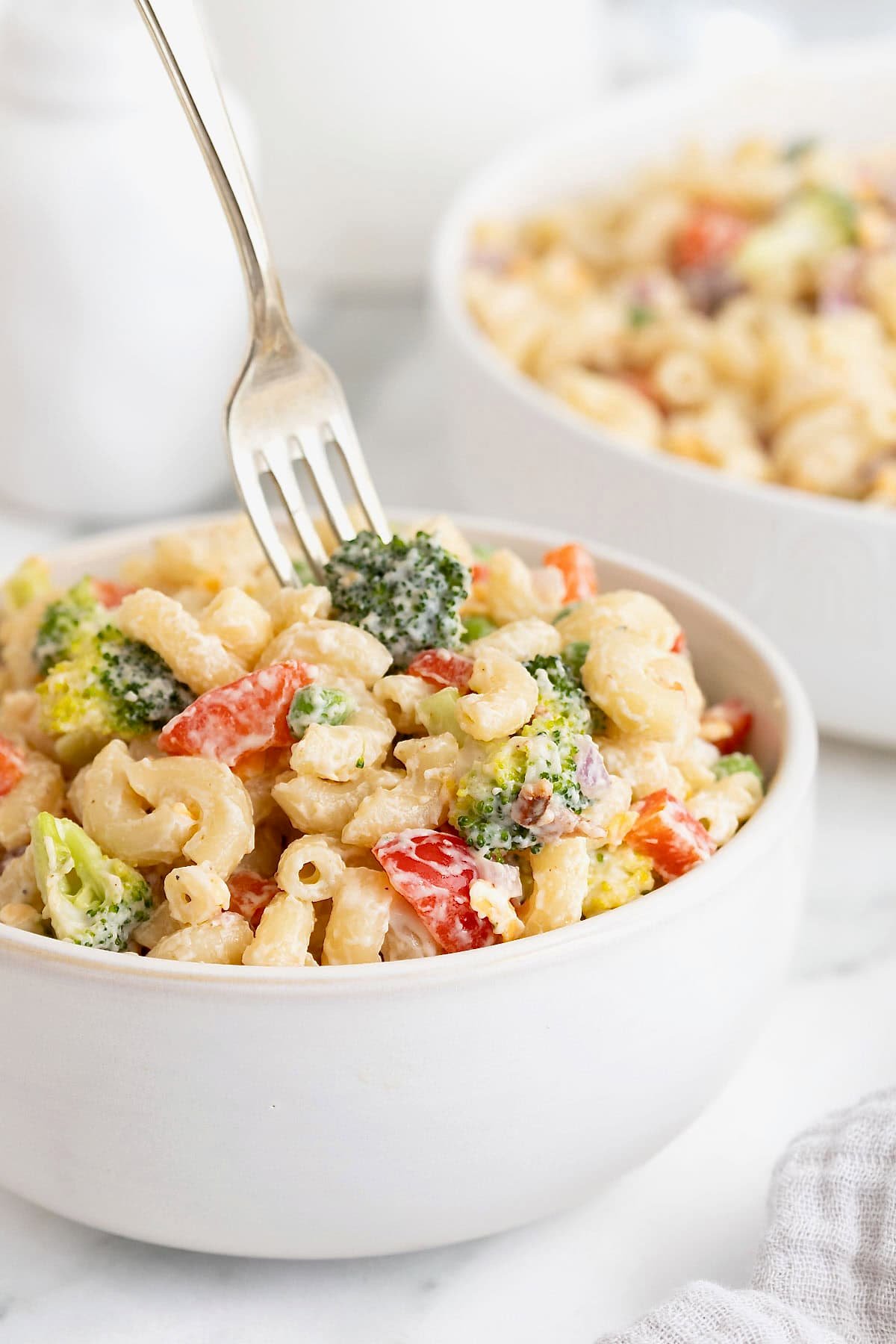 A fork in spearing a small piece of broccoli in a bowl of pasta salad.