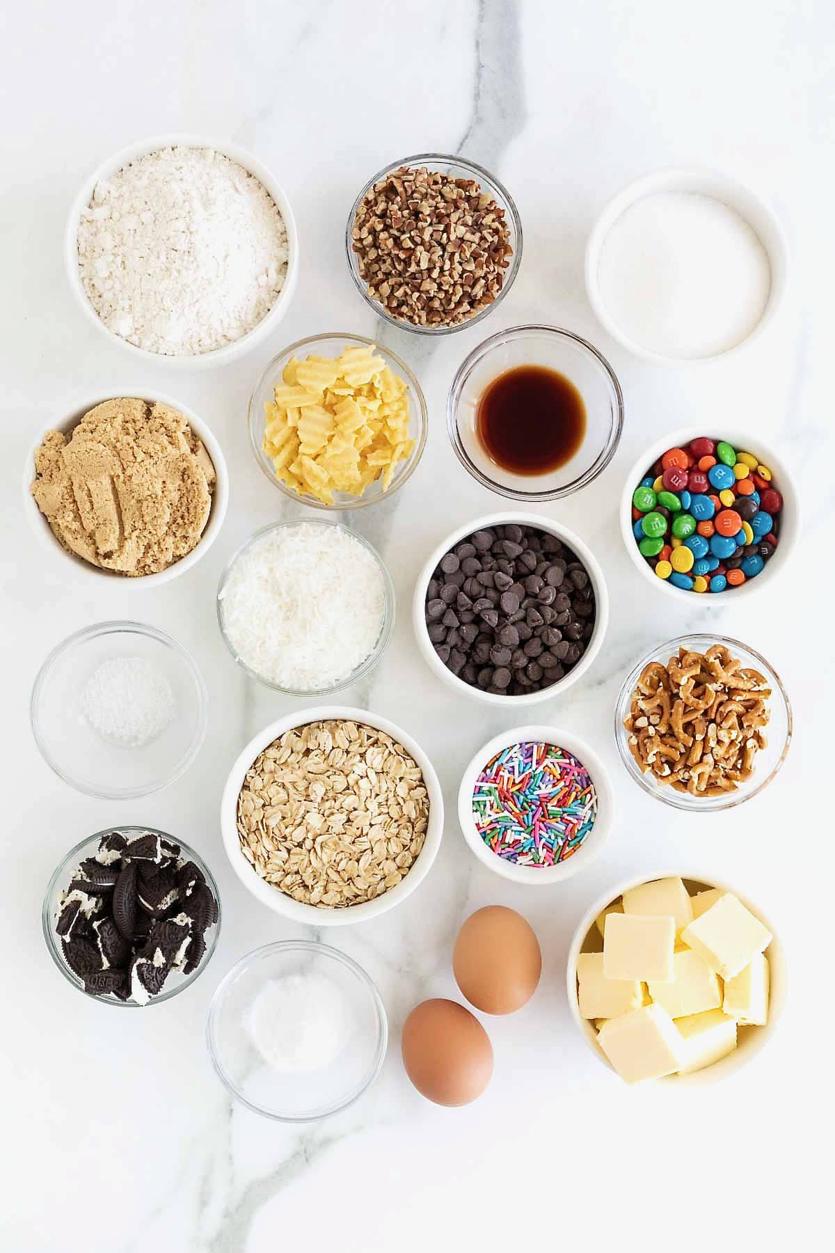 Ingredients to make Kitchen Sink Cookies in small glass dishes on a white marble counter.