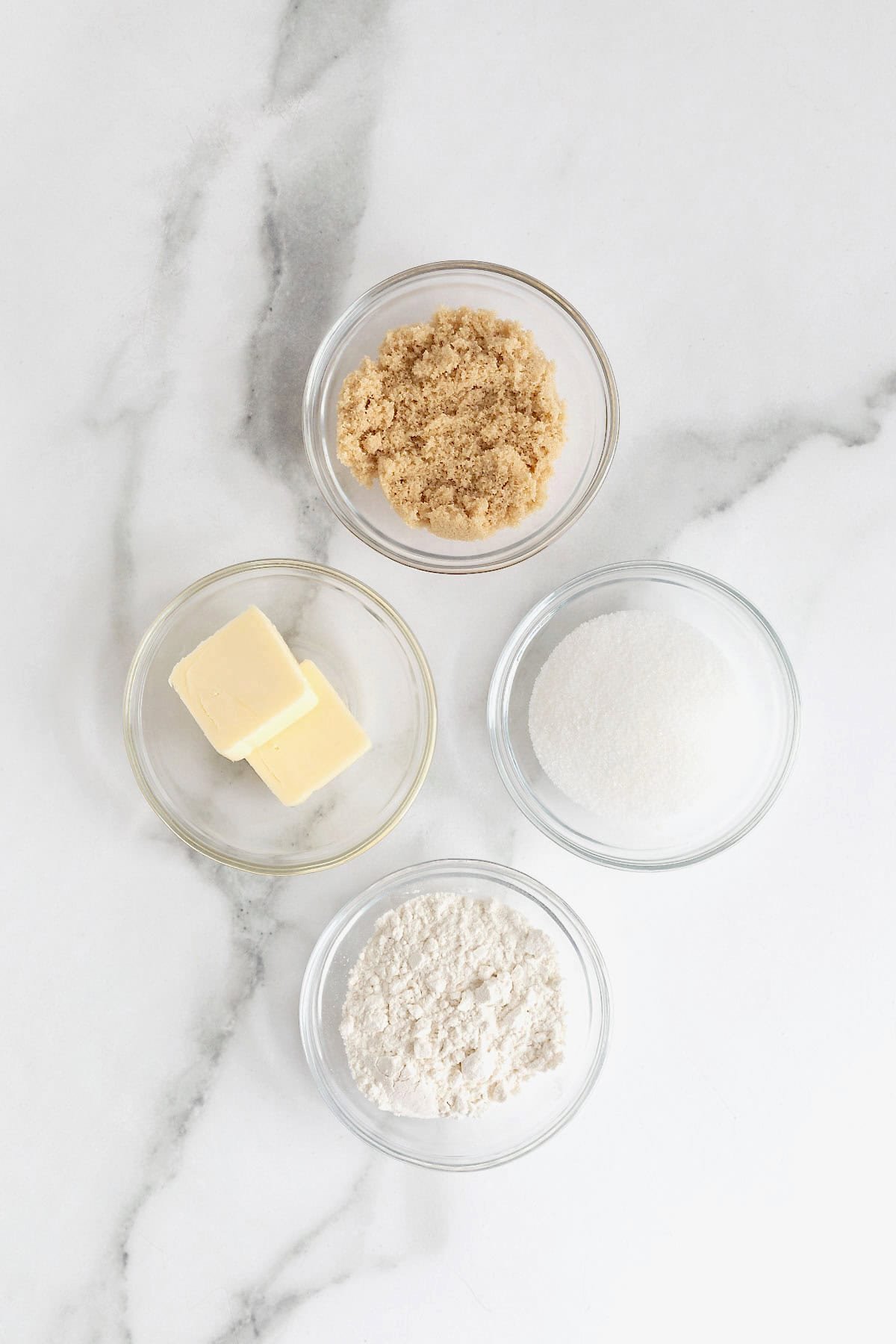 Ingredients to make streusel in small glass dishes on a white marble counter.