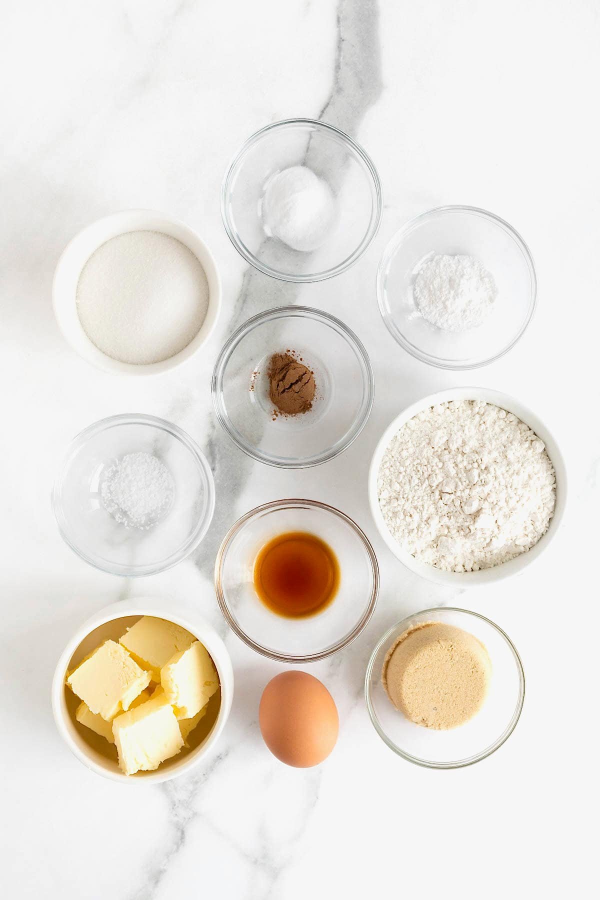 Ingredients to make classic snickerdoodle cookies in small glass dishes on a white marble counter.