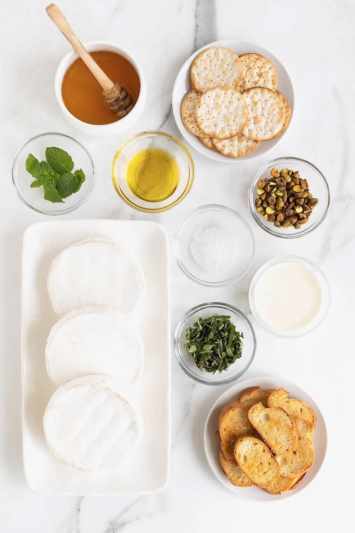 Ingredients to make whipped brie in small white dishes on a white marble counter.