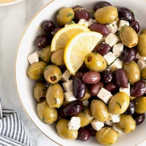 A gold rimmed white serving bowl filled with green and purple olives and small cubes of feta.