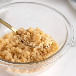A spoonful of streusel being lifted from a glass bowl.