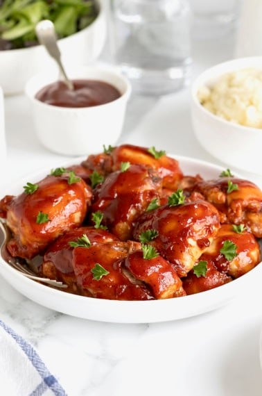 A large white rimmed serving plate of barbecue chicken thighs.