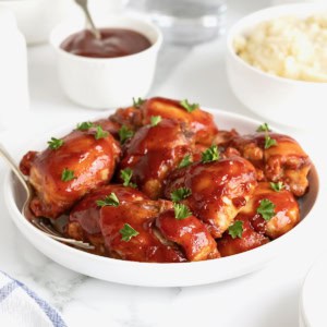 A large white rimmed serving plate of barbecue chicken thighs.