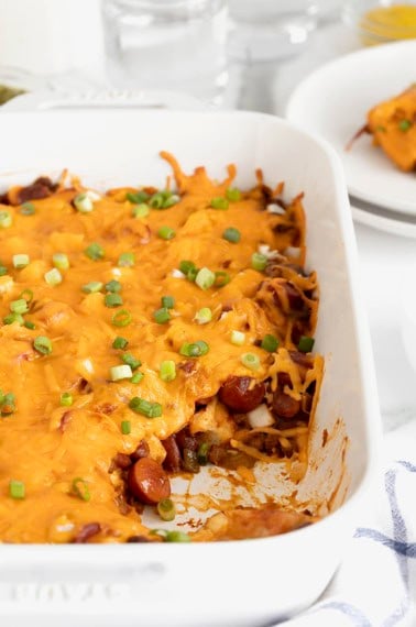 A rectangular white casserole dish of chili cheese dog casserole.