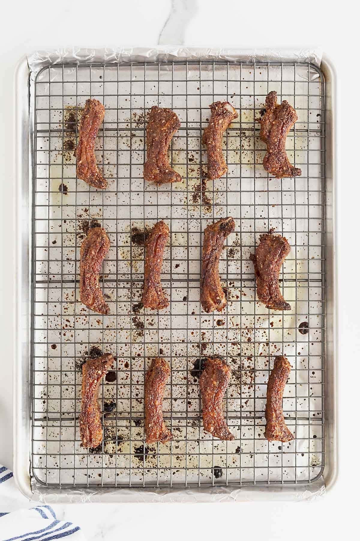 12 baby back ribs on a wire rack over a prepared baking sheet.