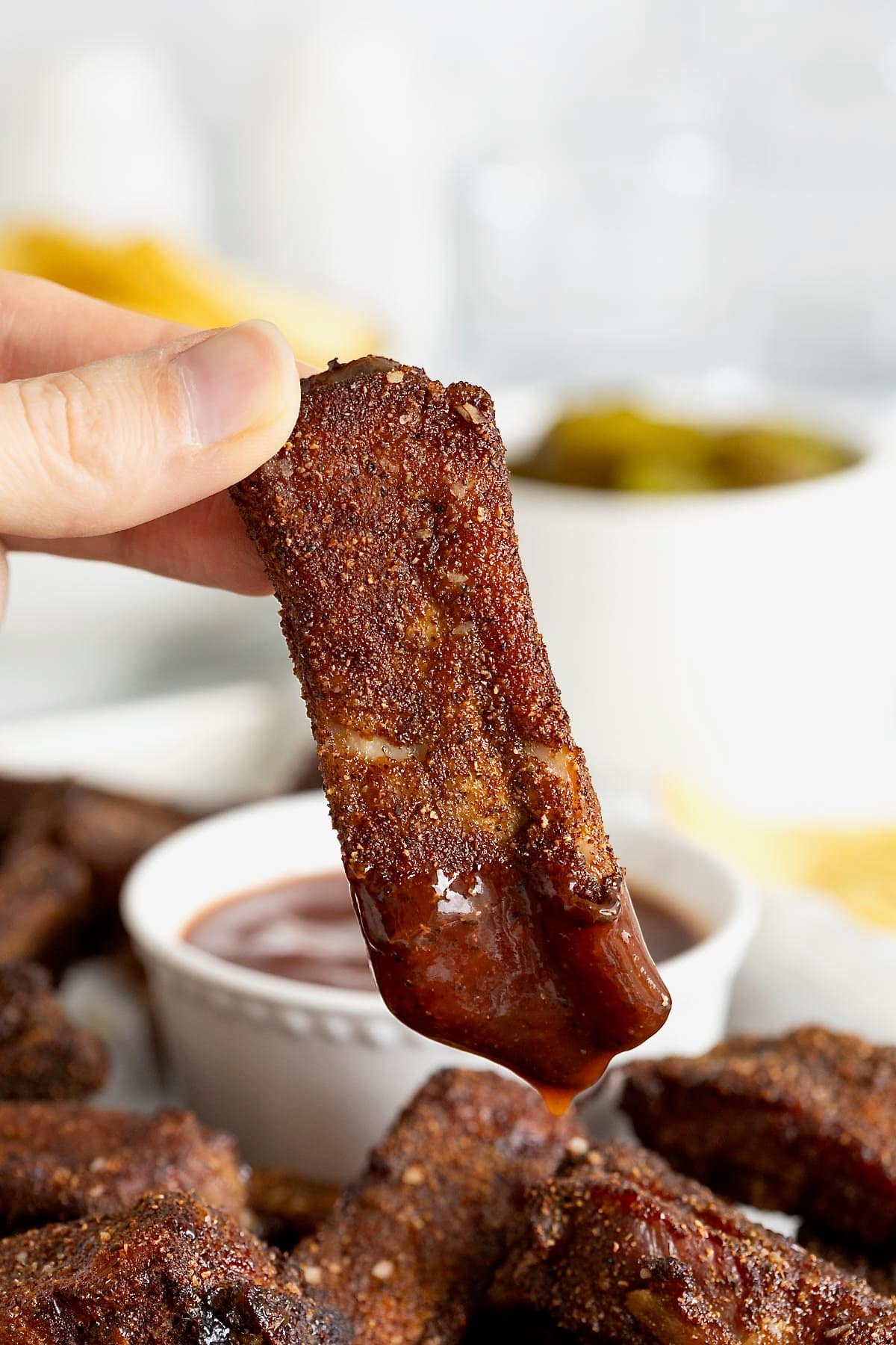 A baby back rib being dipped in barbecue sauce.