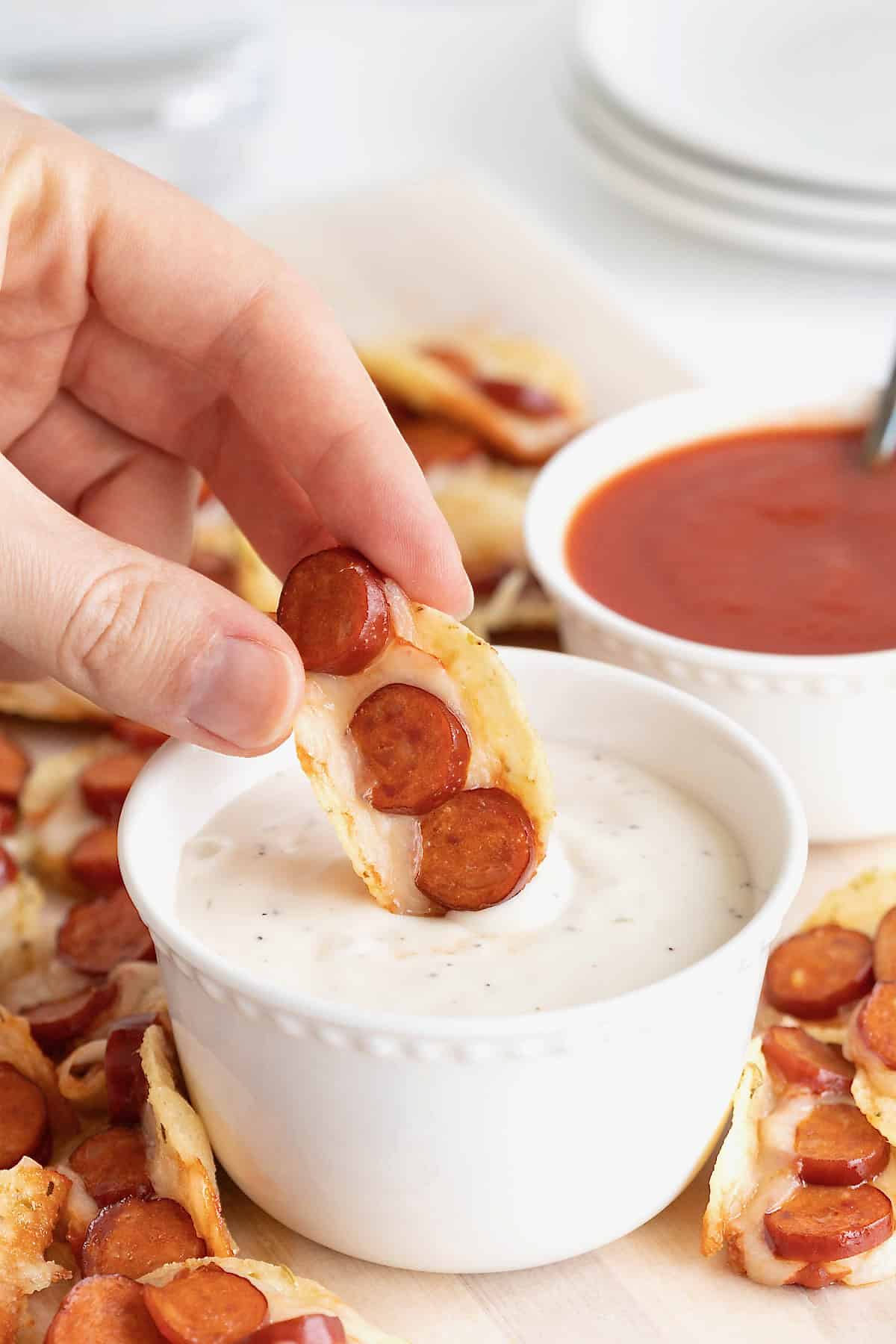A pizza taco bite being dipped in ranch dressing in a small white dish.