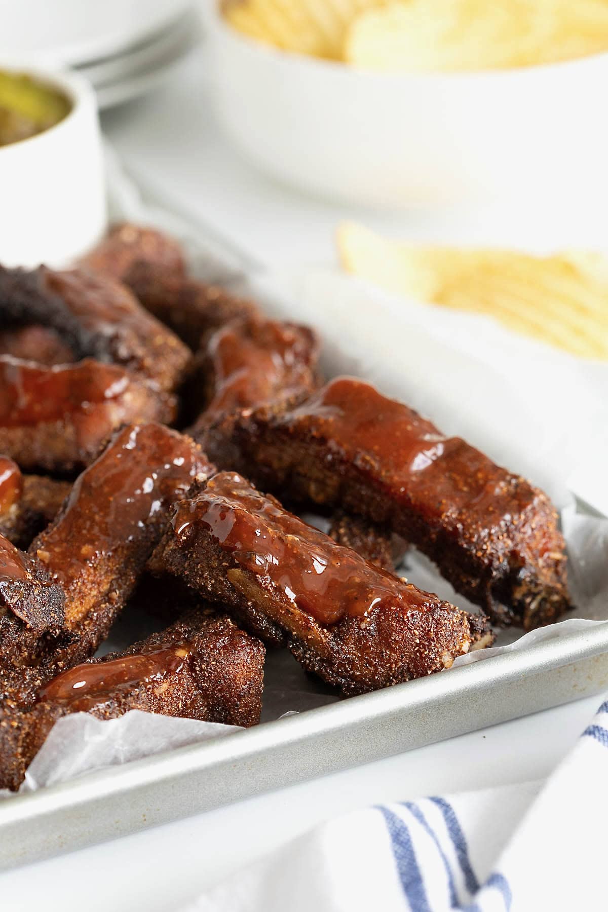 A pile of baby back ribs drizzled with barbecue sauce on a parchment lined aluminum rimmed baking sheet.
