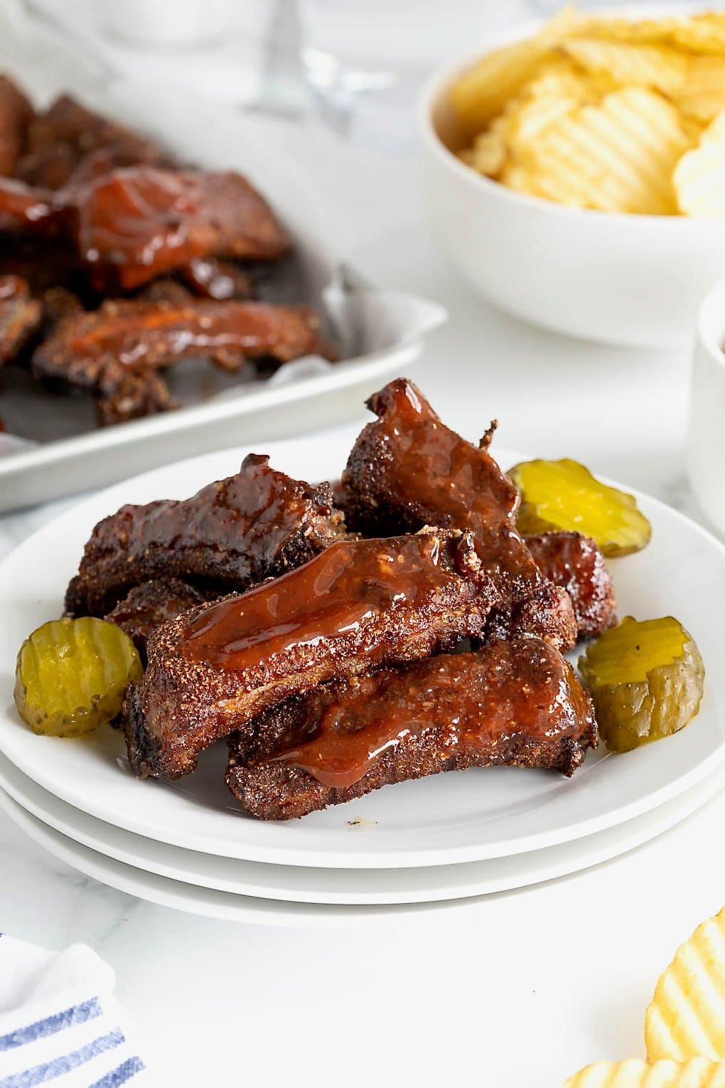 A plate of baby back ribs with barbecue sauce and pickle slices.