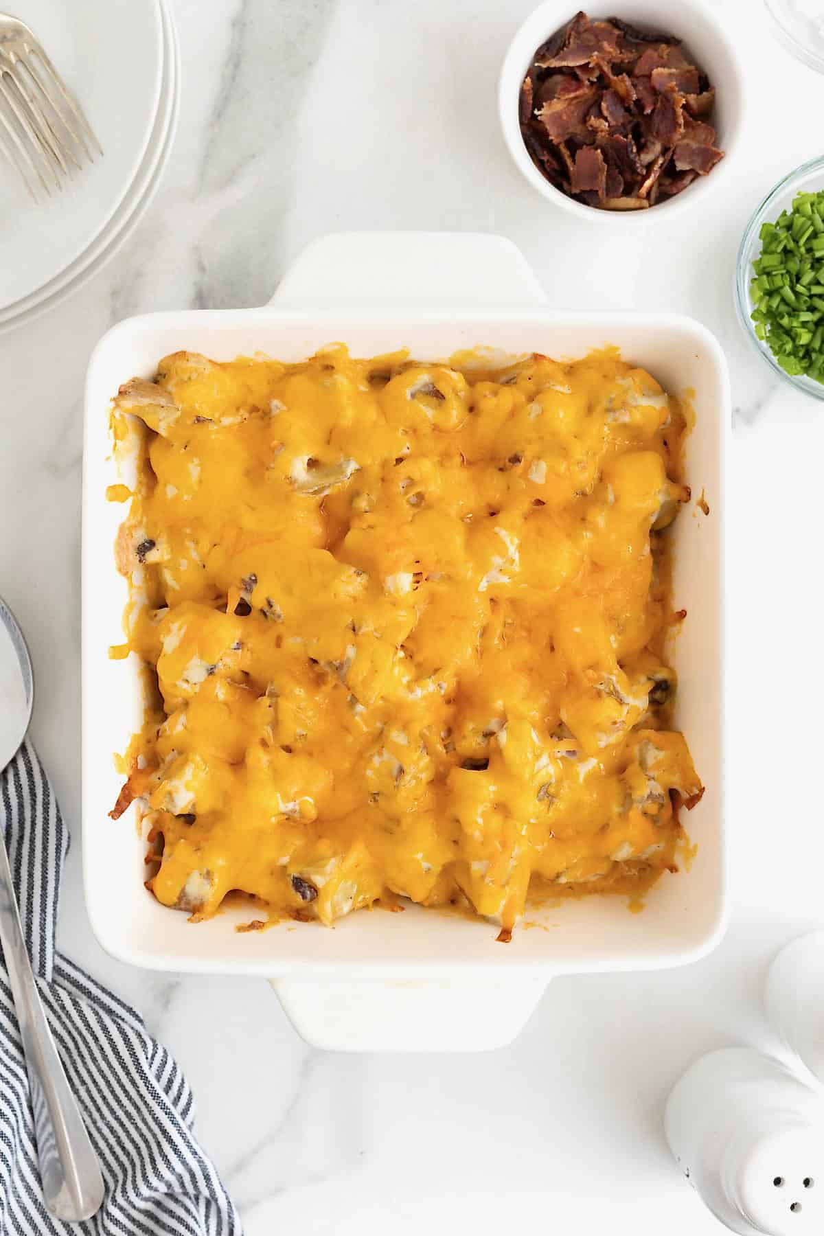 Twice baked potato casserole in a square white glass baking dish on a white marble counter.