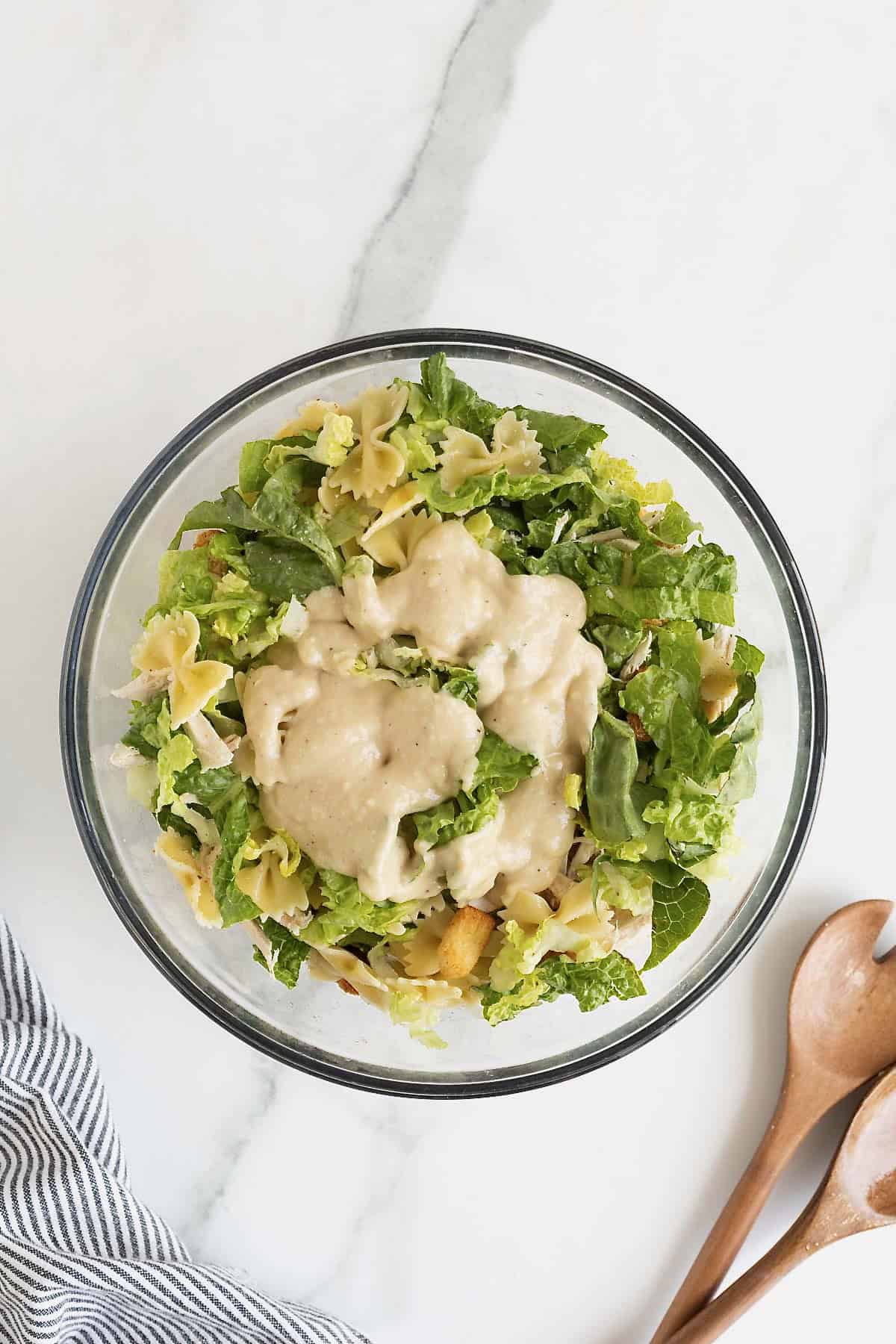 Caesar dressing on a salad in a large glass mixing bowl.