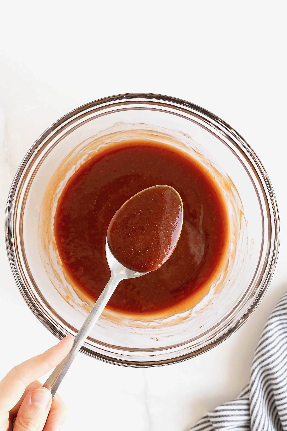A spoon dipped into a glass mixing bowl of barbecue sauce.