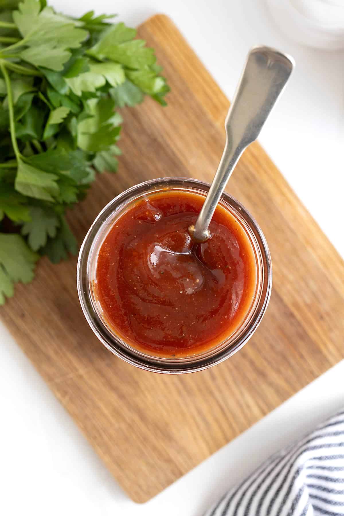 A wide mouth glass jar of barbecue sauce with a spoon sticking out of it.