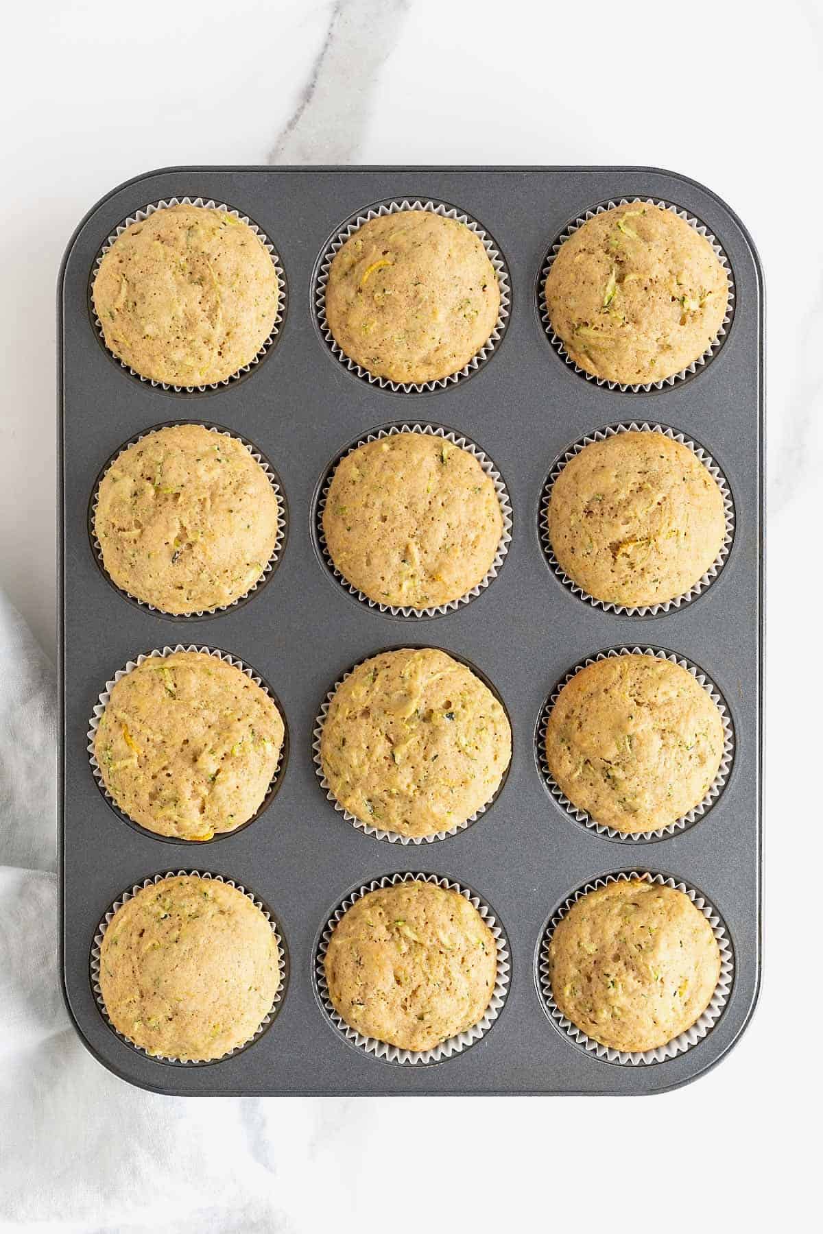 A dark aluminum 12-cup muffin pan of zucchini muffins.