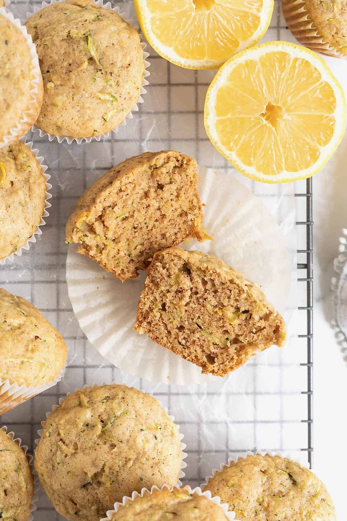 A zucchini muffin cut in half on a parchment lined wire cooling rack. To the top right of the muffin is half a lemon.