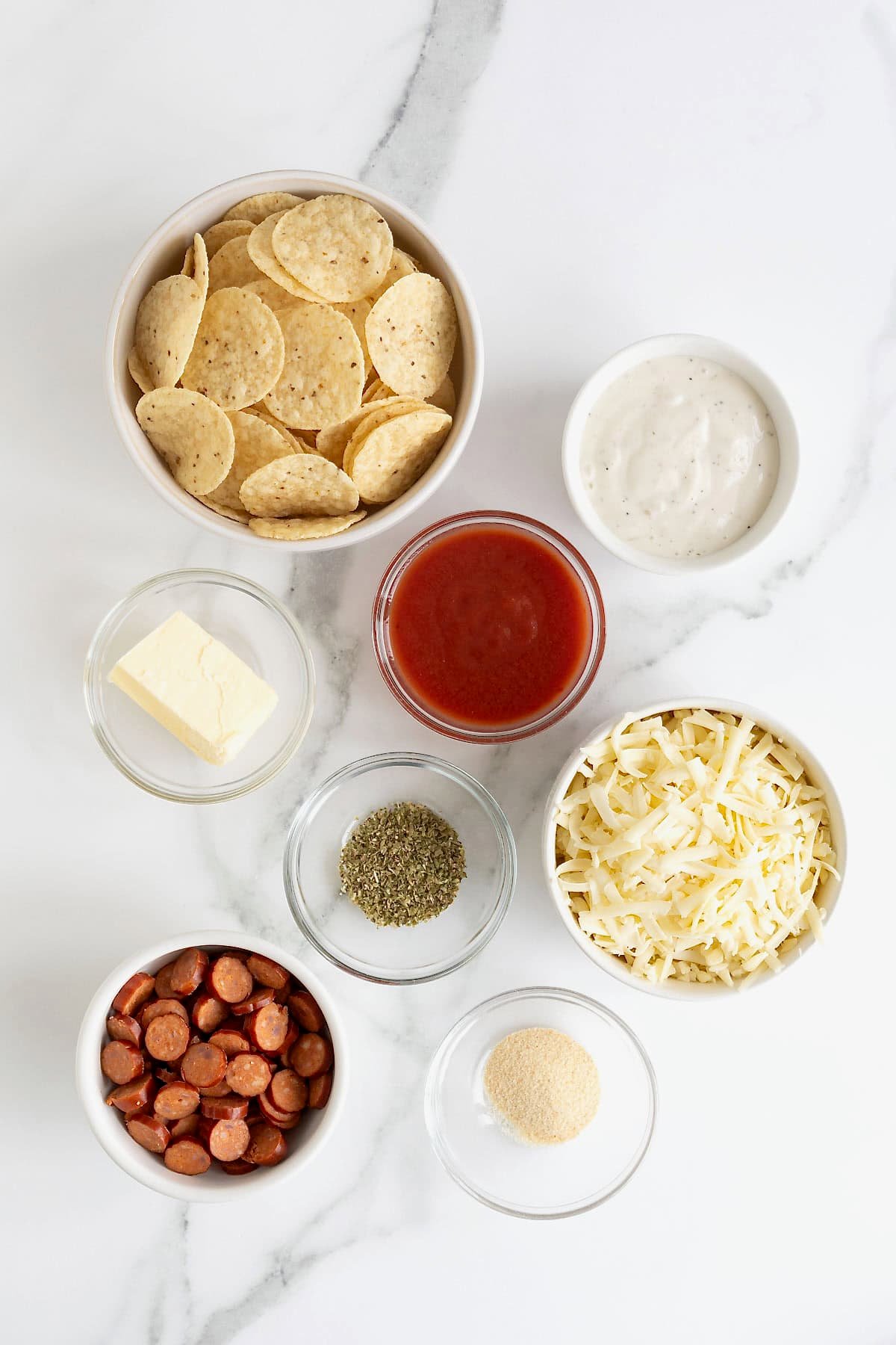Ingredients to make pizza taco bites in small glass dishes on a white marble counter.