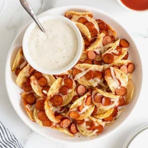 A large rimmed white serving plate piled with pizza taco bites. There is a small white dish of ranch dipping sauce.