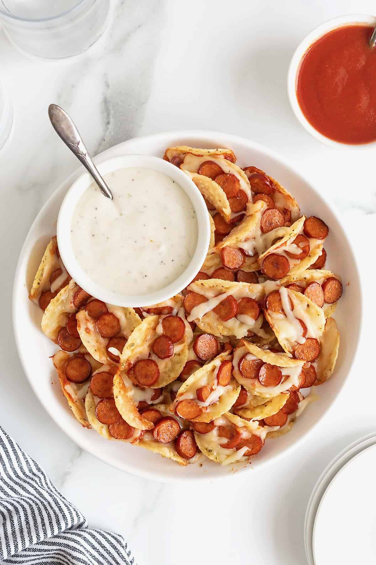 A large rimmed white serving plate piled with pizza taco bites. There is a small white dish of ranch dipping sauce.