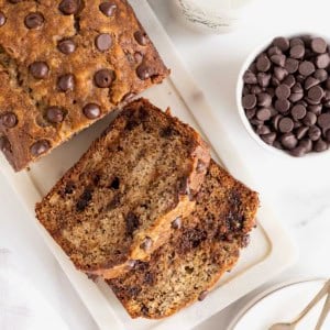 A loaf of brown butter banana bread studded with chocolate chips on a white cutting board.