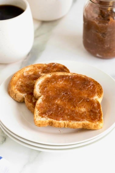 Two pieces of toast spread with grape jam on a white plate.