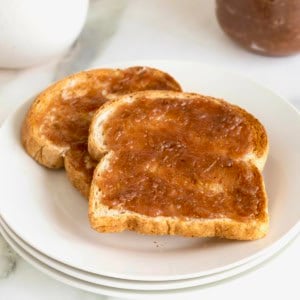 Two pieces of toast spread with grape jam on a white plate.