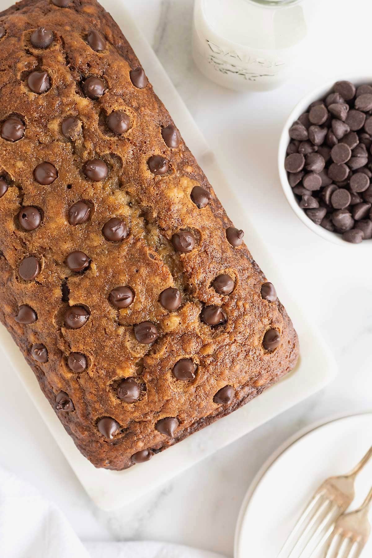 A loaf of brown butter banana bread studded with chocolate chips on a white surface.