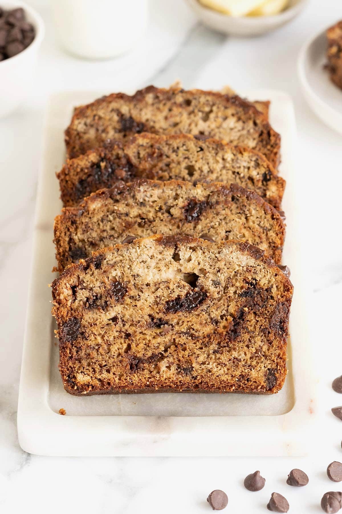 Four slices of chocolate chip brown butter banana bread on a white cutting board.